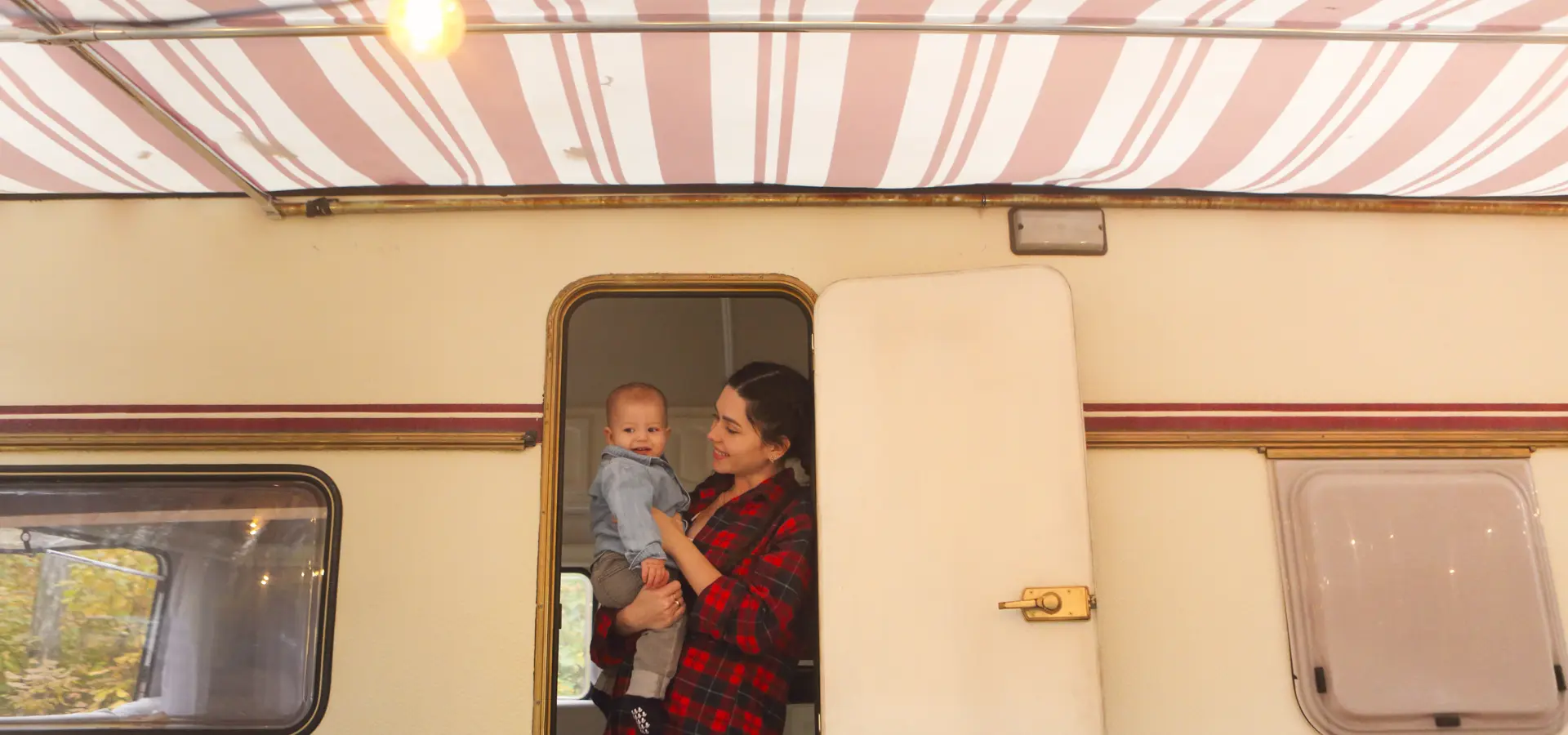 Vrouw met haar baby in de handen voor een caravan